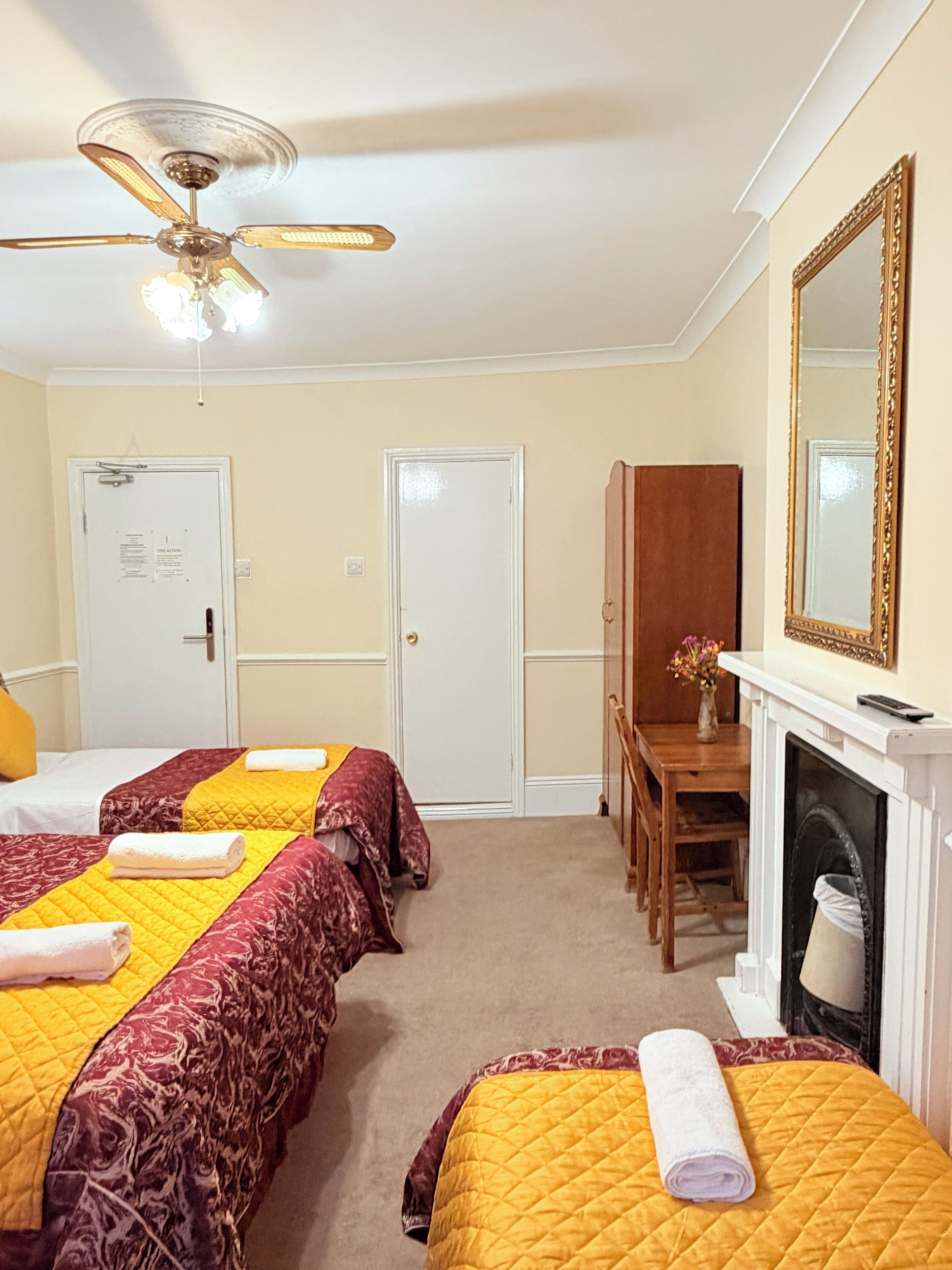 Una habitación de hotel con dos camas, ventilador de techo, chimenea y un espejo en la pared.