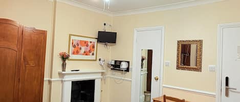 A hotel room with a bed, a desk, a chair, a television, a fireplace, and a wardrobe.
