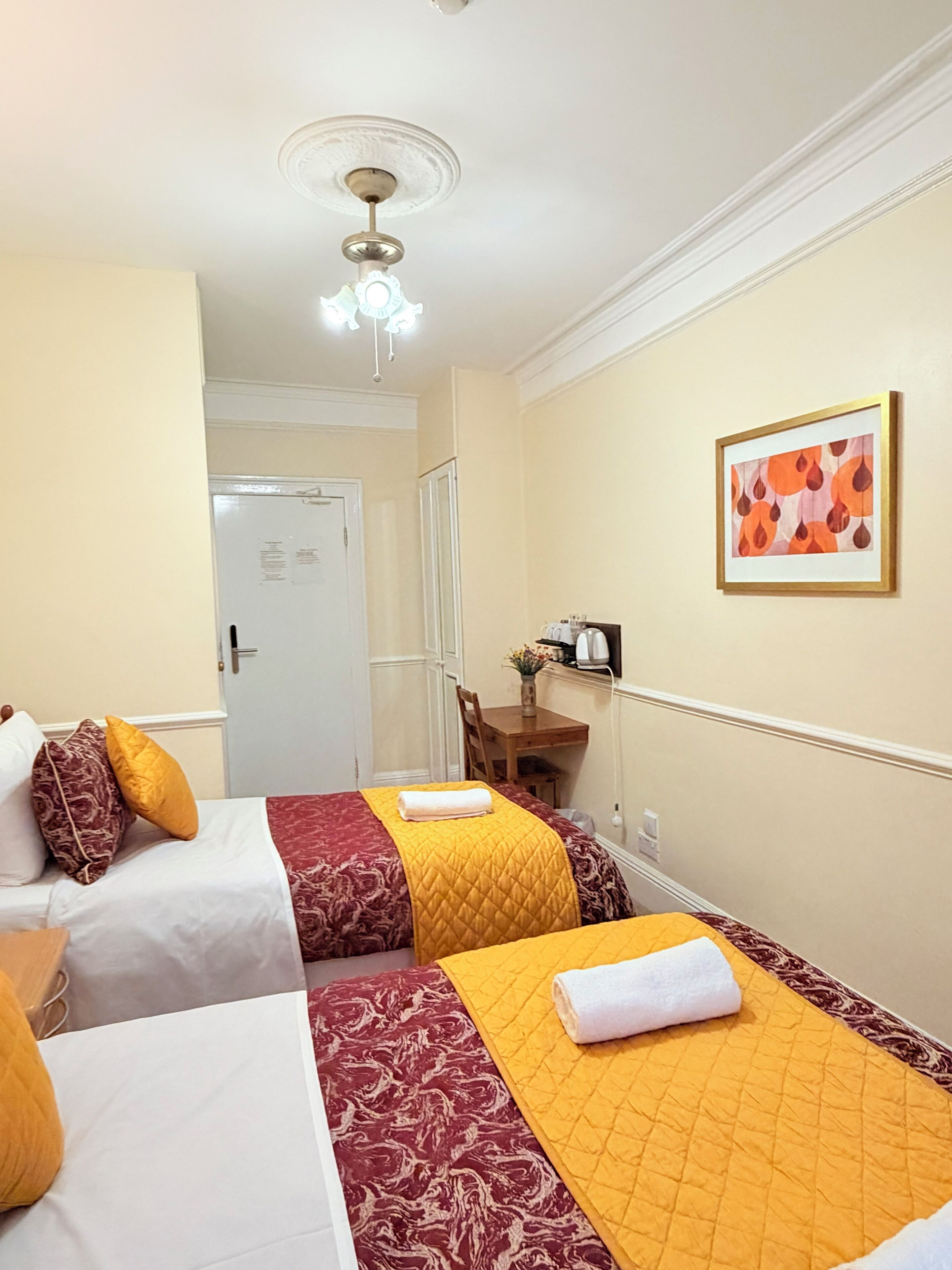 A hotel room with two beds, a desk, a chair, a ceiling fan, and a framed picture on the wall.