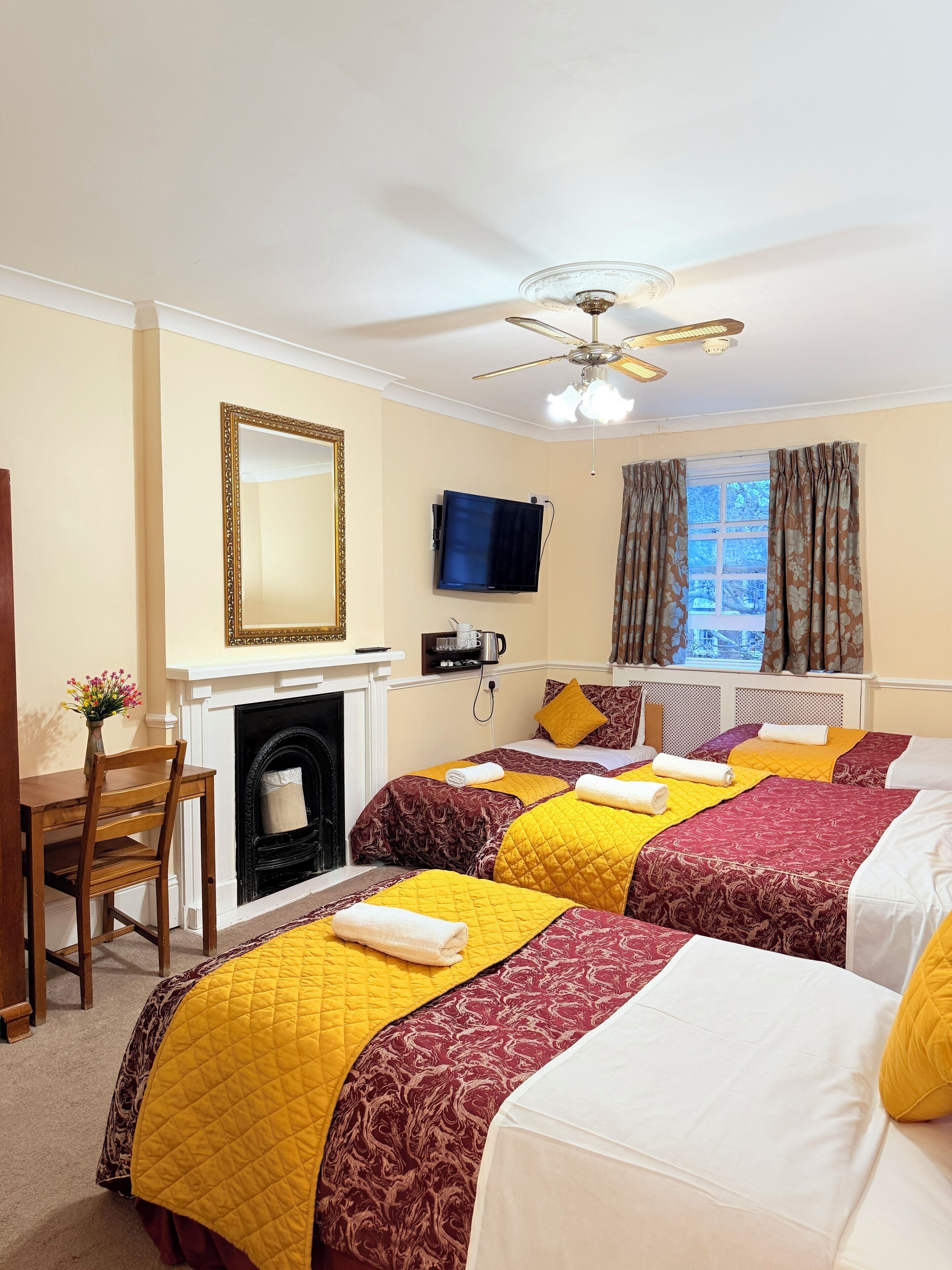 A hotel room with two beds, a fireplace, a television mounted on the wall, and a window with curtains.