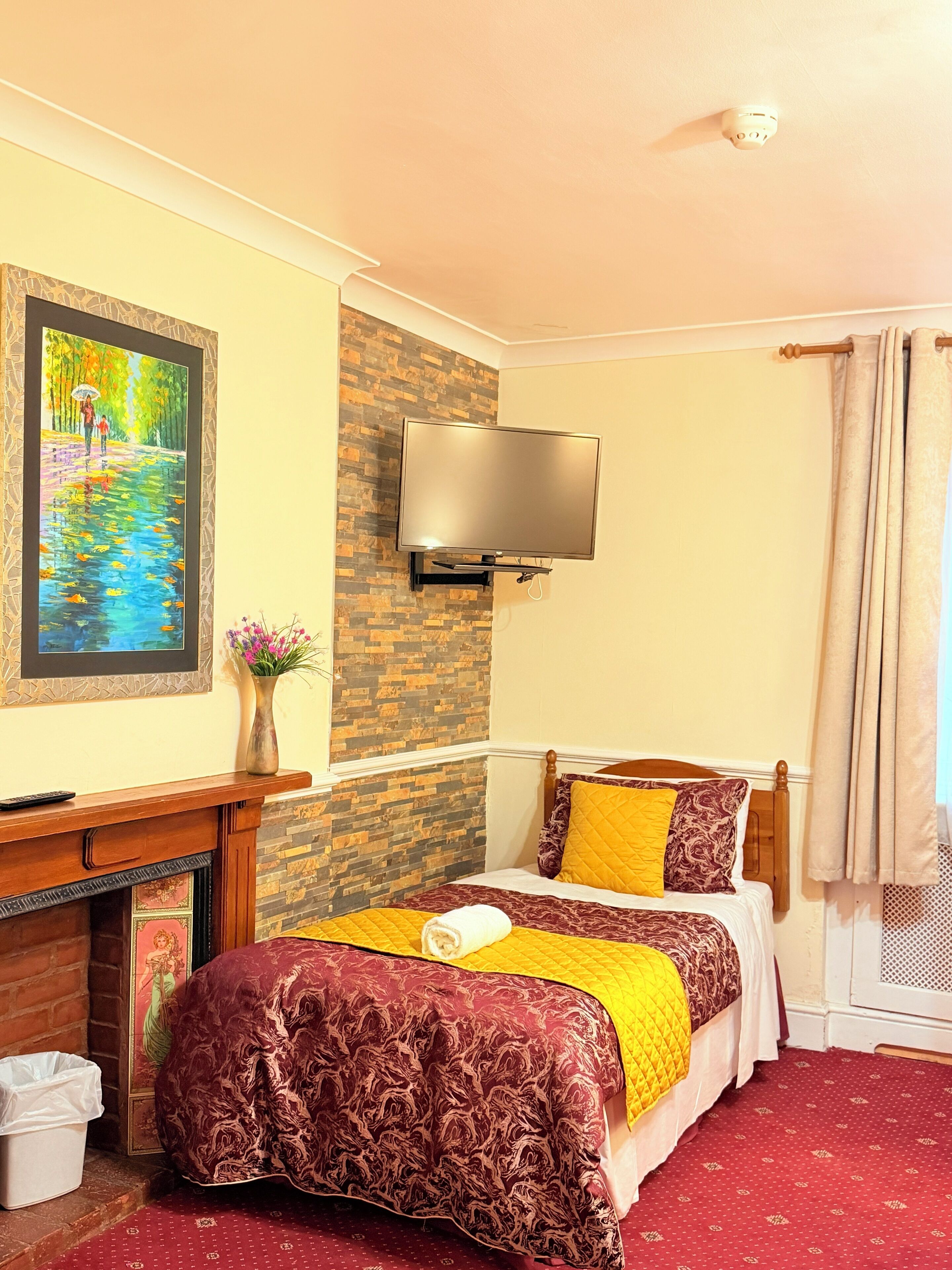 A hotel room with a bed, a painting, a TV, and a fireplace.