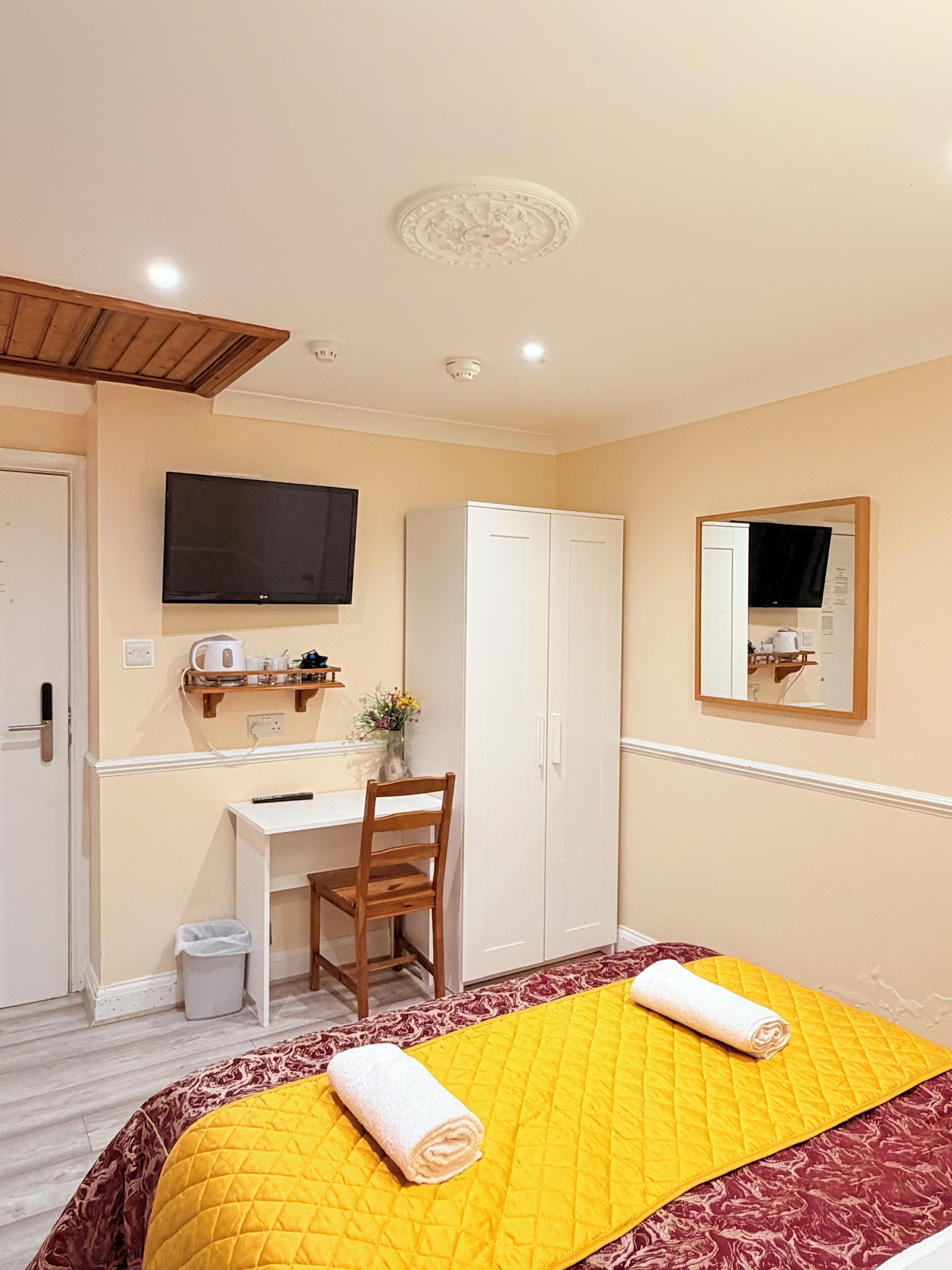 A hotel room with a bed, a desk, a chair, a wardrobe, a television, and a mirror.
