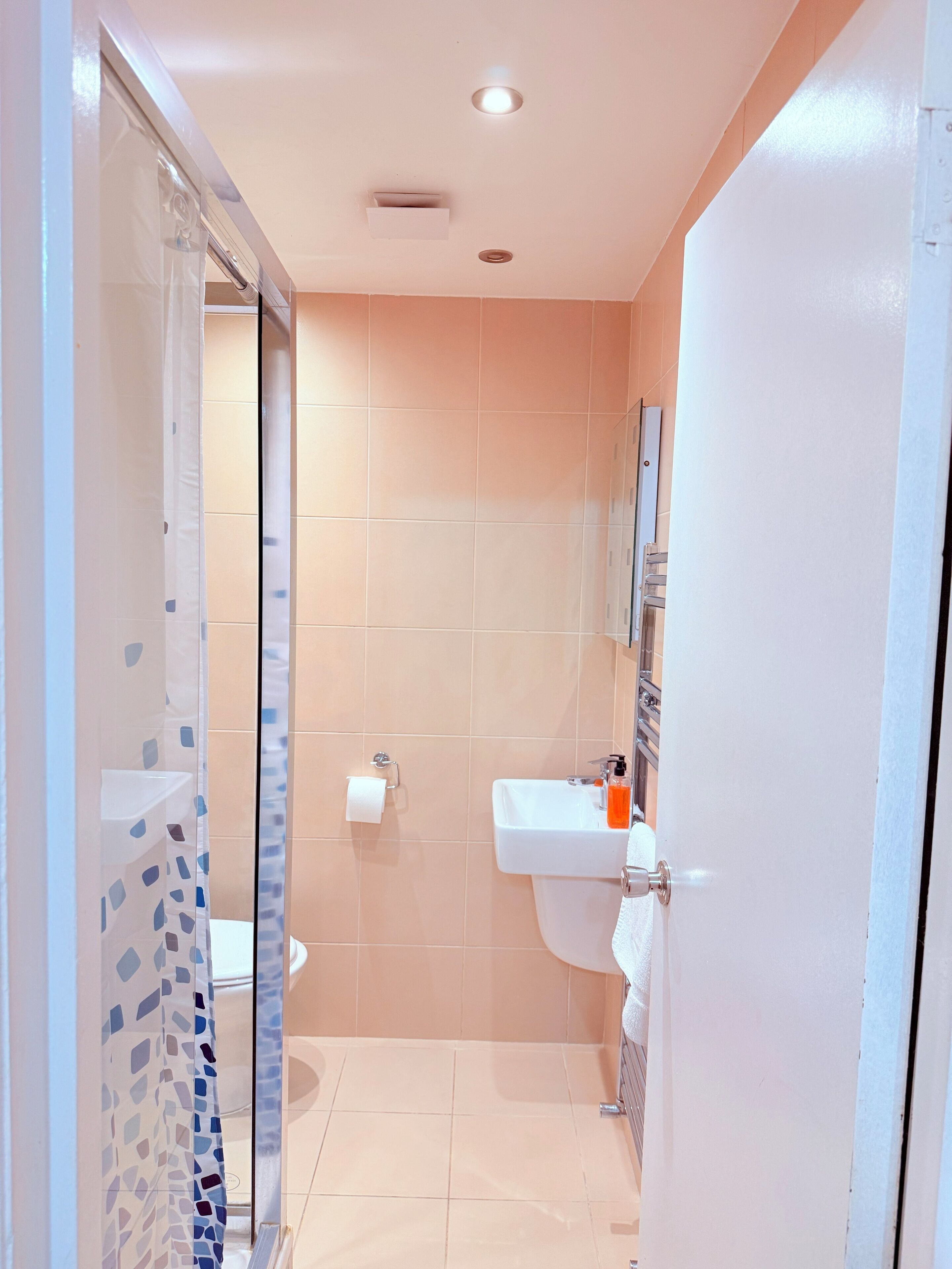 Een badkamer met een douchecabine van glas, een wit wastafeltje en een toilet.