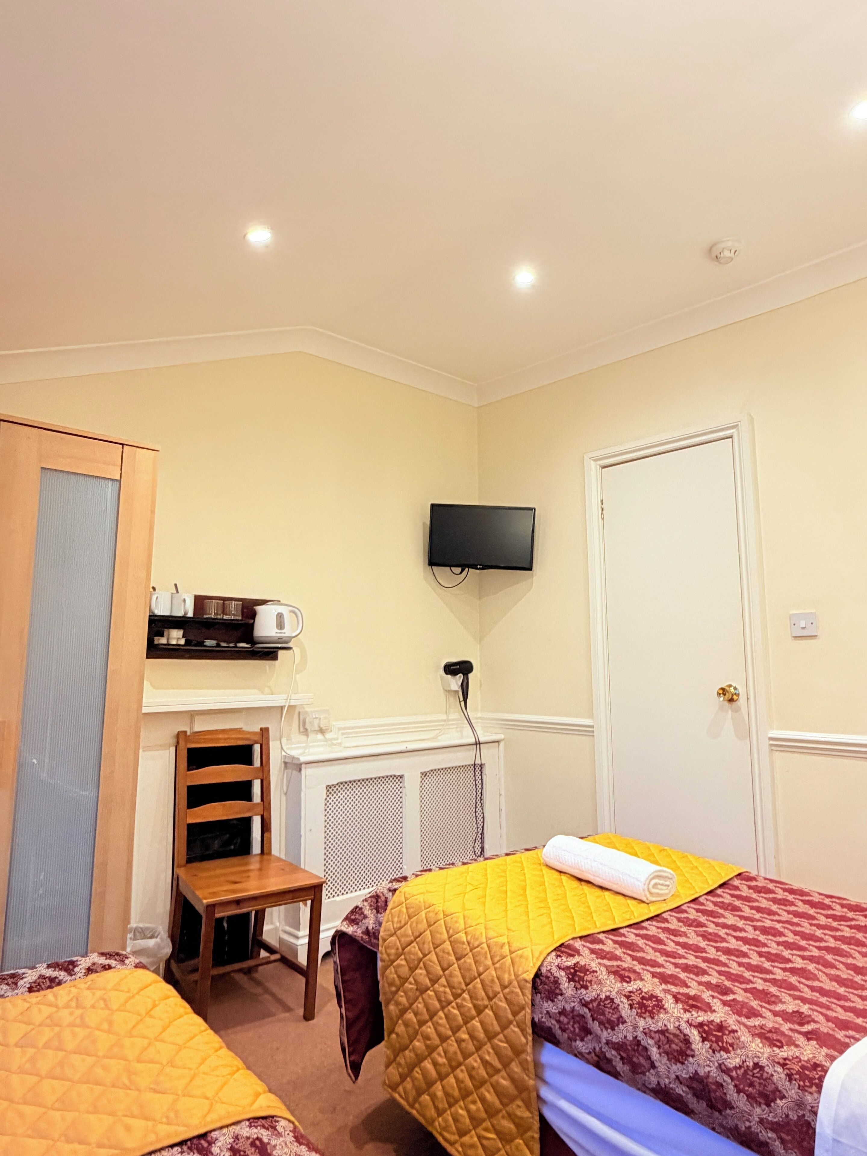 A hotel room with two beds, a television mounted on the wall, a small table, and a chair.