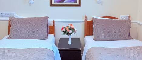 A hotel room with two beds, a nightstand with a vase of flowers, and a framed picture on the wall.