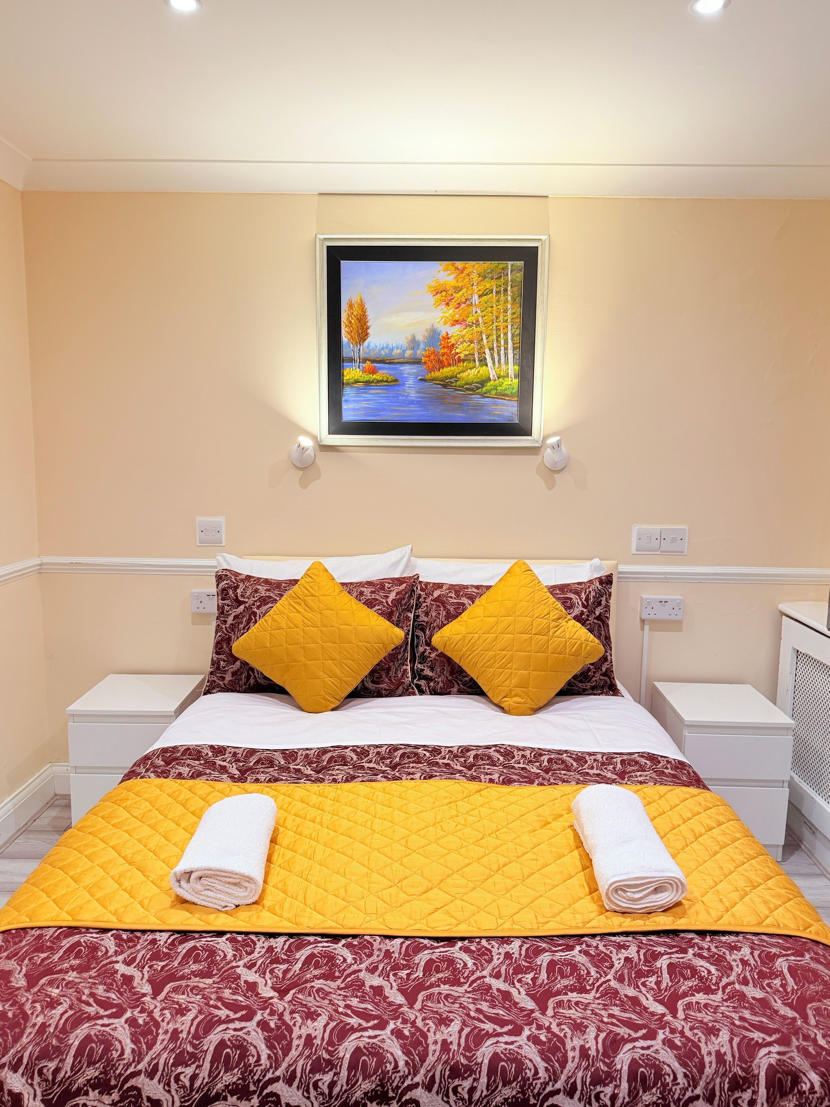 A neatly made bed with a yellow quilt, two pillows, and a white towel.