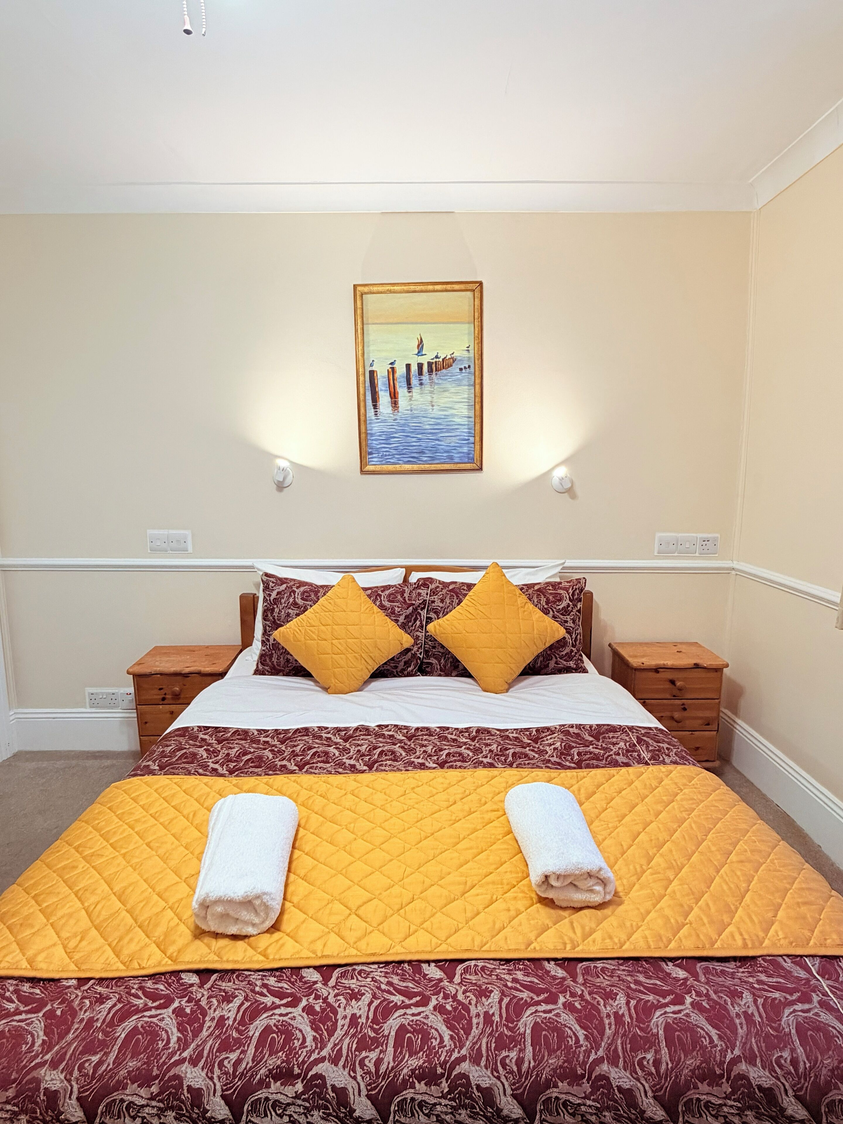 A neatly made bed with a yellow quilt, two matching pillows, and two towels.