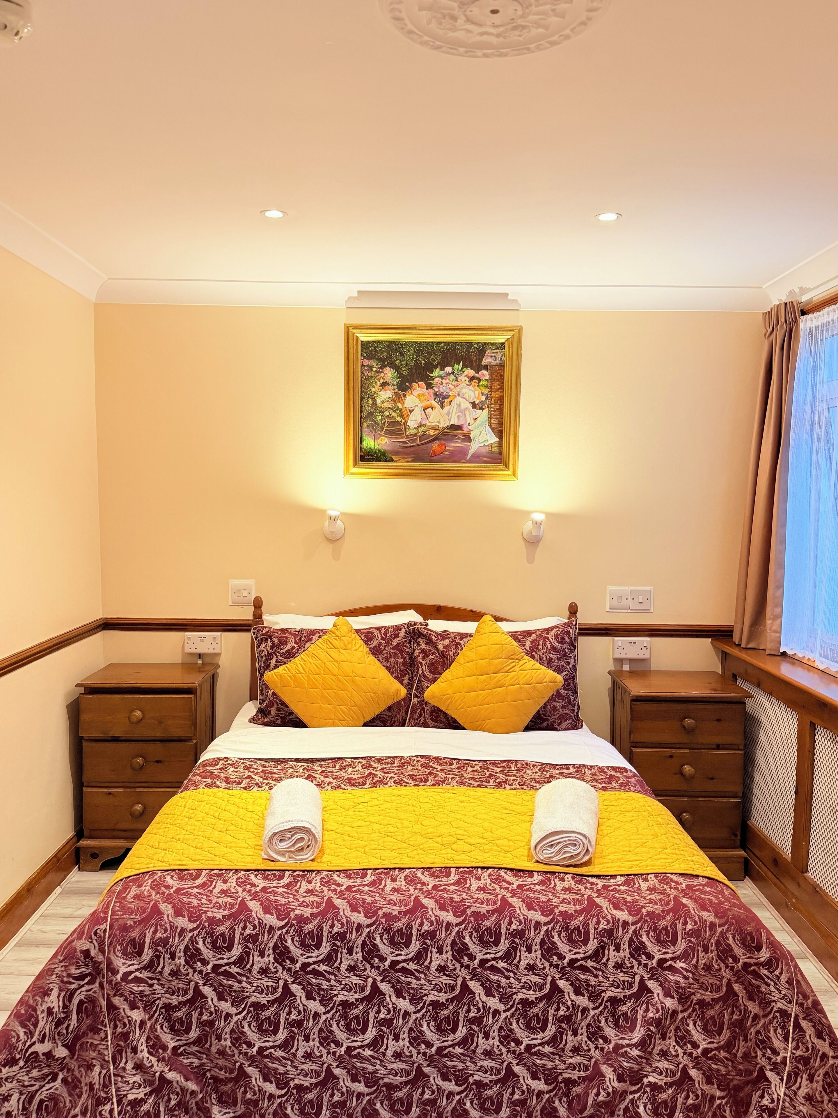 A neatly arranged bedroom with a bed, two bedside tables, and a painting above the bed.
