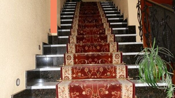 A staircase with a red carpet and black steps, leading to a landing with a metal railing. - Hostal Restaurante San Poul (Consuegra)