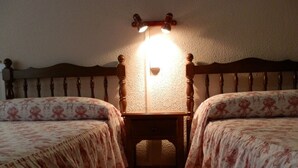A bedroom with two beds, a nightstand, and a wall-mounted lamp. - Hostal Restaurante San Poul (Consuegra)