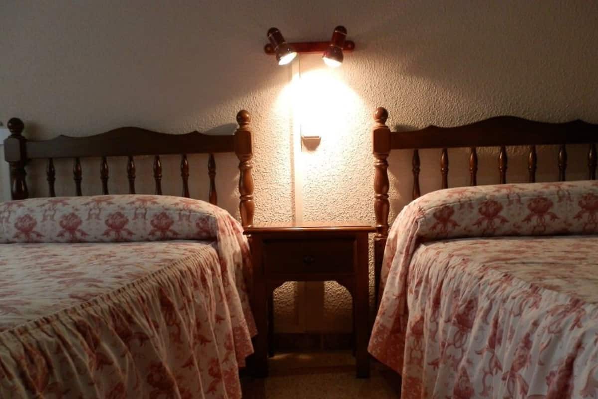Une chambre avec deux lits, une table de chevet et une lampe fixée au mur.