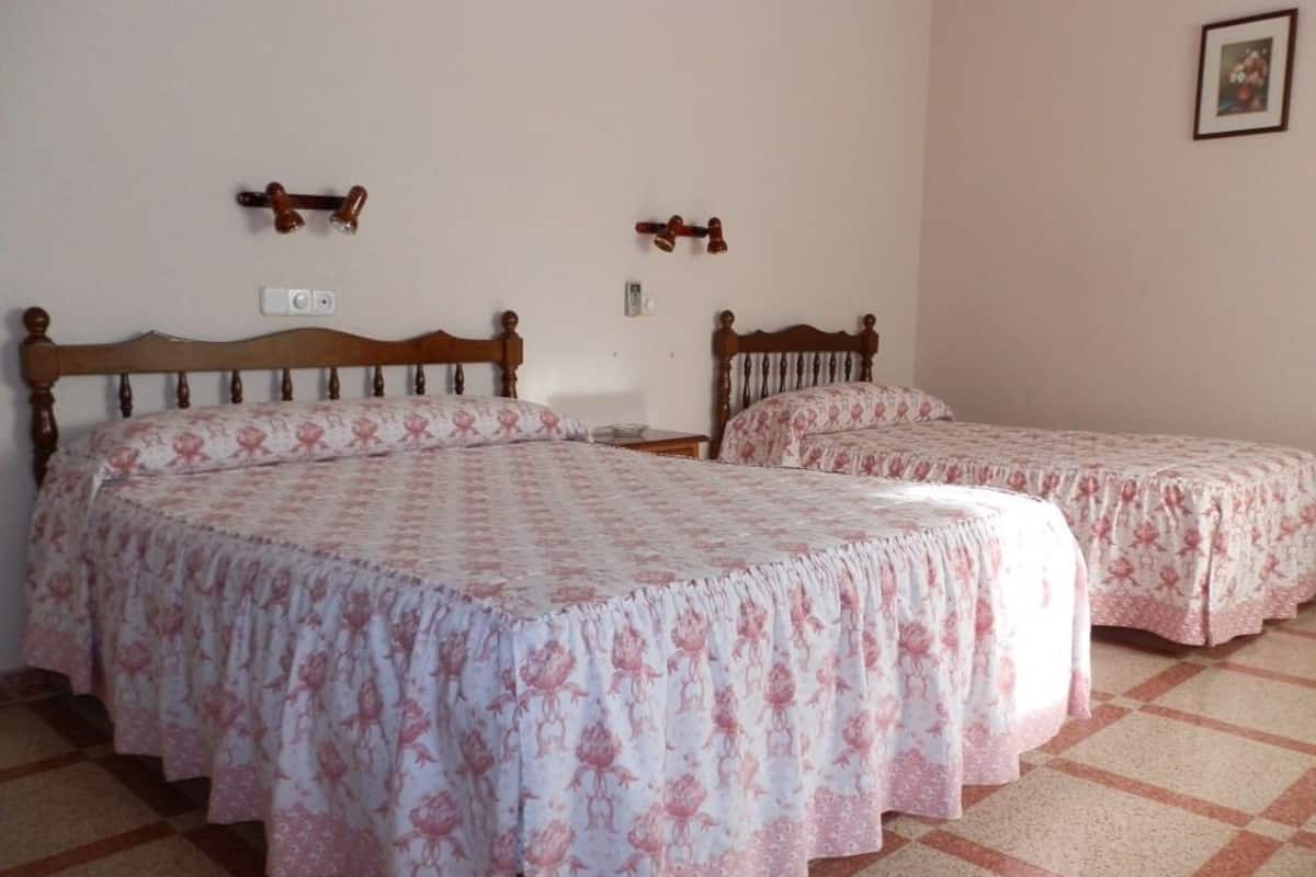 Une chambre avec deux lits en bois, chacun recouvert d’une couvre-lit à motifs floraux. Des appliques murales éclairent la pièce et un tableau encadré est accroché au mur.