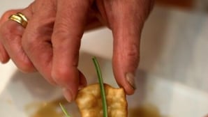 A hand holding a piece of food with green garnish on a plate with sauce. - Hostal Restaurante San Poul (Consuegra)
