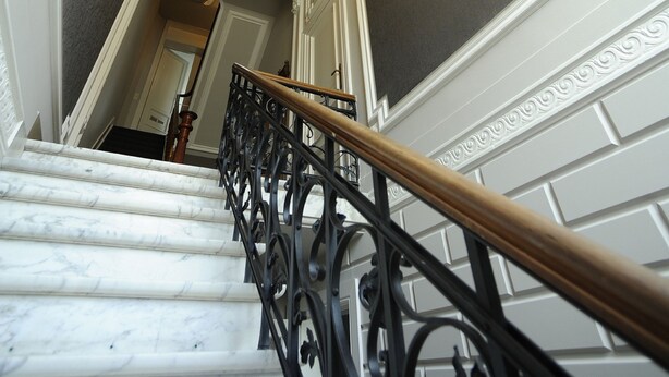 A marble staircase with ornate black railings and a chandelier. - Expo 13 (Ghent)