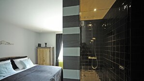 A modern bedroom with a large bed, a wooden wardrobe, and a separate bathroom with a glass shower enclosure. - Expo 13 (Ghent)