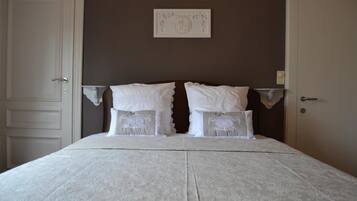 A neatly made bed with white linens and decorative pillows, a framed artwork on the wall, and a door to the left.