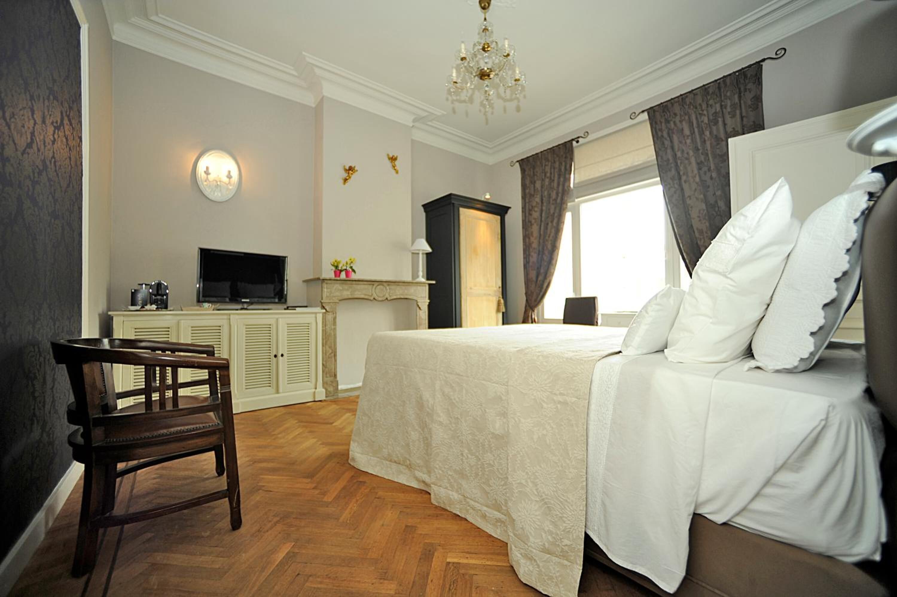 Habitación de hotel con cama, escritorio con televisor, una silla, chimenea y candelabro.