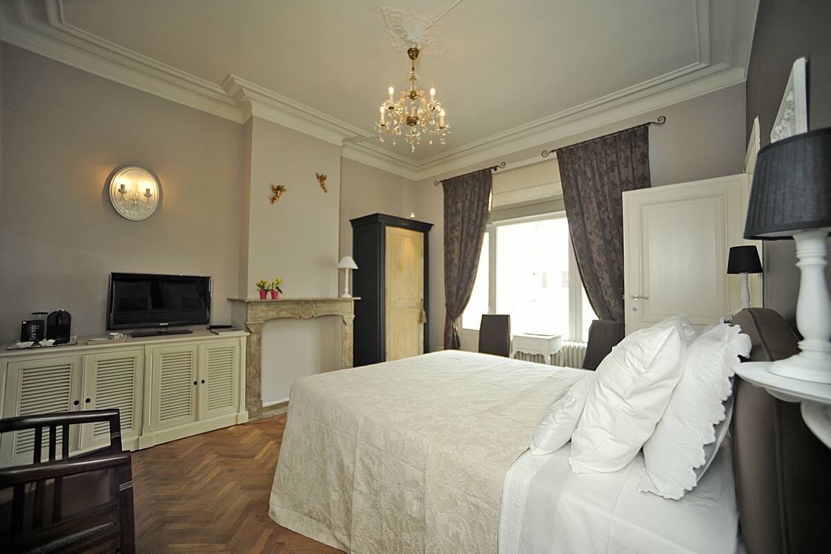 A hotel room with a large bed, a television, a fireplace, and a chandelier.