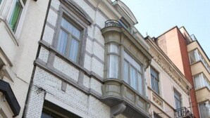 A multi-story building with a corner bay window, large windows, and a visible door with a sign. - Expo 13 (Ghent)