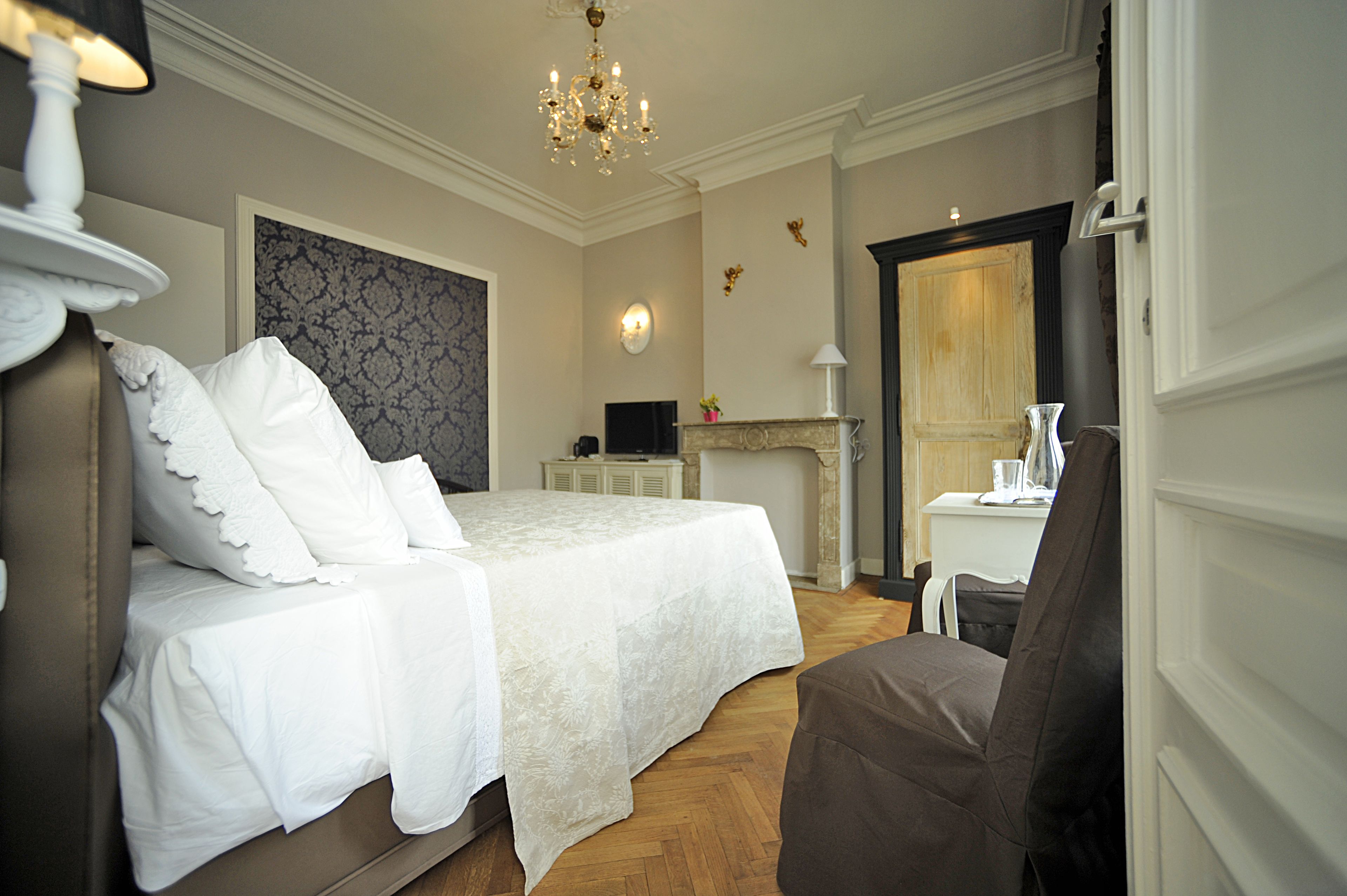 Une chambre d’hôtel avec un grand lit, une chaise, une petite table, une cheminée et un lustre.