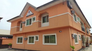 A multi-story building with a sign reading "DC Suites." It features multiple windows, some with bars, and several potted plants. - DC Bar & Suites (Lagos)