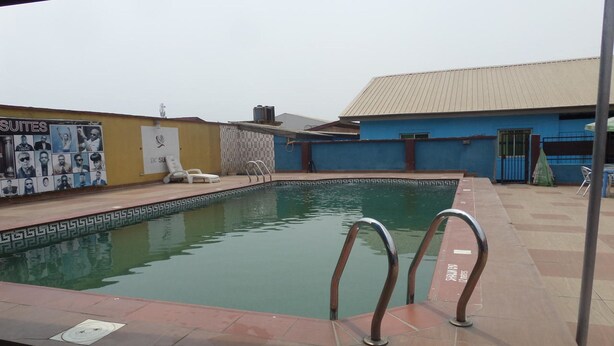 A swimming pool with metal handrails, a tiled deck, and a building with a blue facade in the background. - DC Bar & Suites (Lagos)