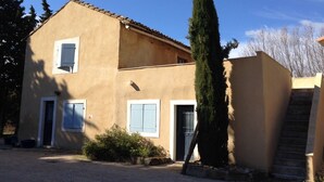 A two-story house with a beige exterior, a tiled roof, and a small front yard with a tall tree and a staircase leading to the entrance. - Clos St Pierre de Fraisse (Avignon)
