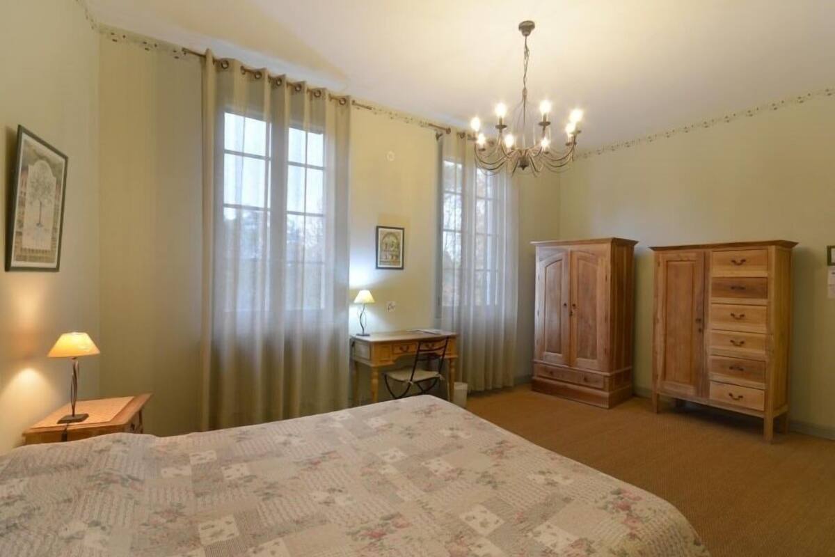 A bedroom with a bed, a desk, a chair, a wardrobe, and a chandelier.
