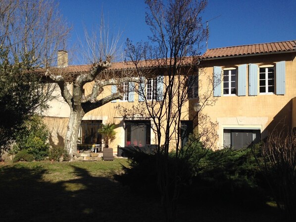 A two-story house with a tiled roof, a large tree in the front yard, and a small garden area. - Clos St Pierre de Fraisse (Avignon)