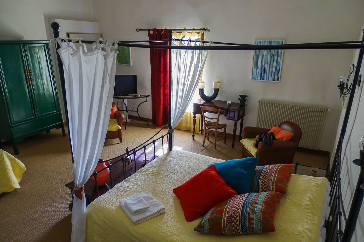 A bedroom with a four-poster bed, a desk, a chair, and a green wardrobe.