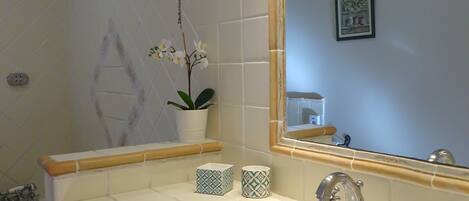 A bathroom with a white sink, a mirror, a potted orchid, and a framed picture on the wall.