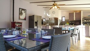 A dining area with a glass table and wicker chairs, a kitchen in the background, and a 'WELCOME' sign on the wall. - Clos St Pierre de Fraisse (Avignon)