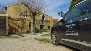 A black car parked in front of a yellow building with a tree and a gravel path. - Clos St Pierre de Fraisse (Avignon)