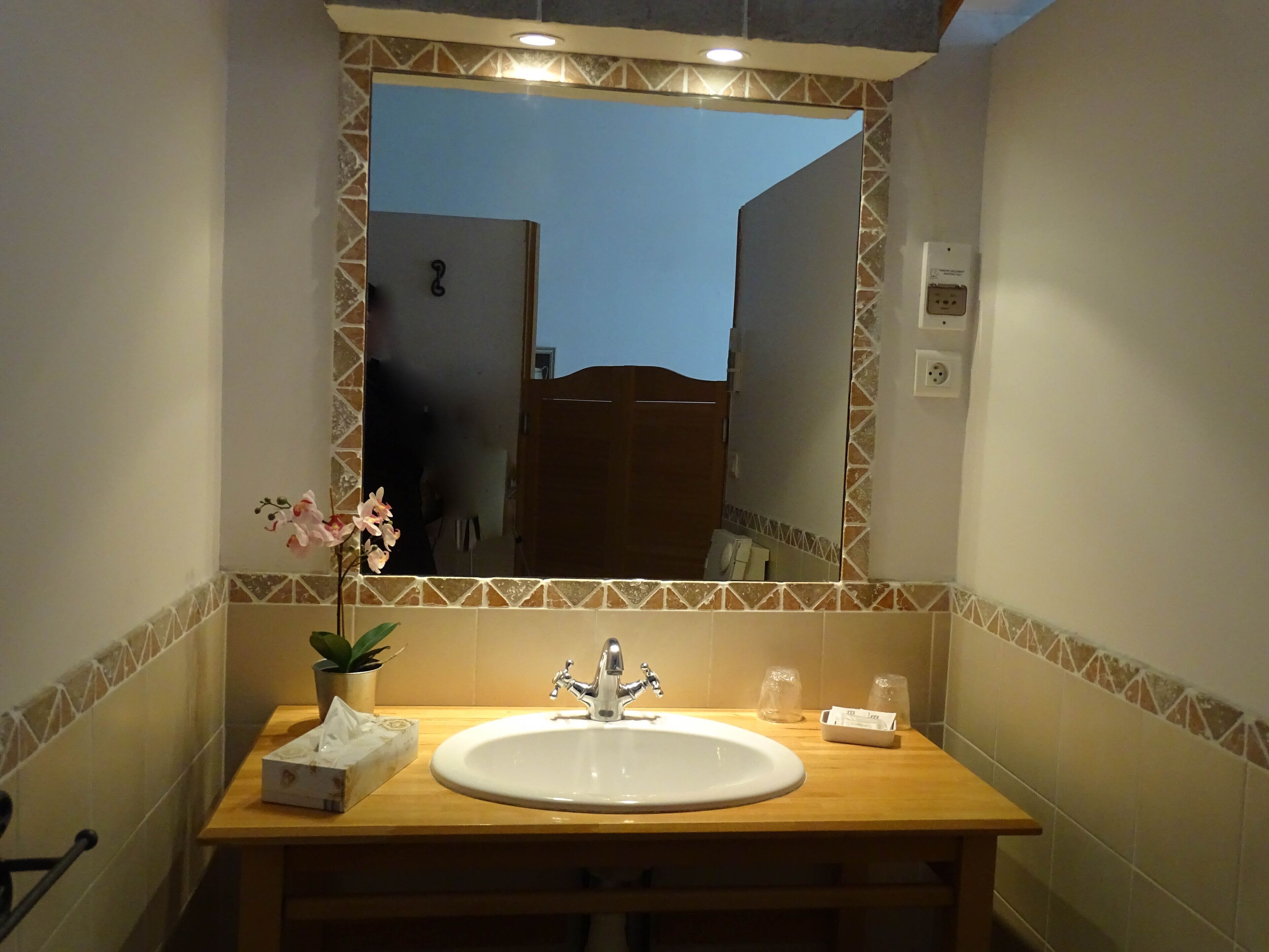 A bathroom with a wooden vanity, a white sink, a mirror, and a potted orchid.