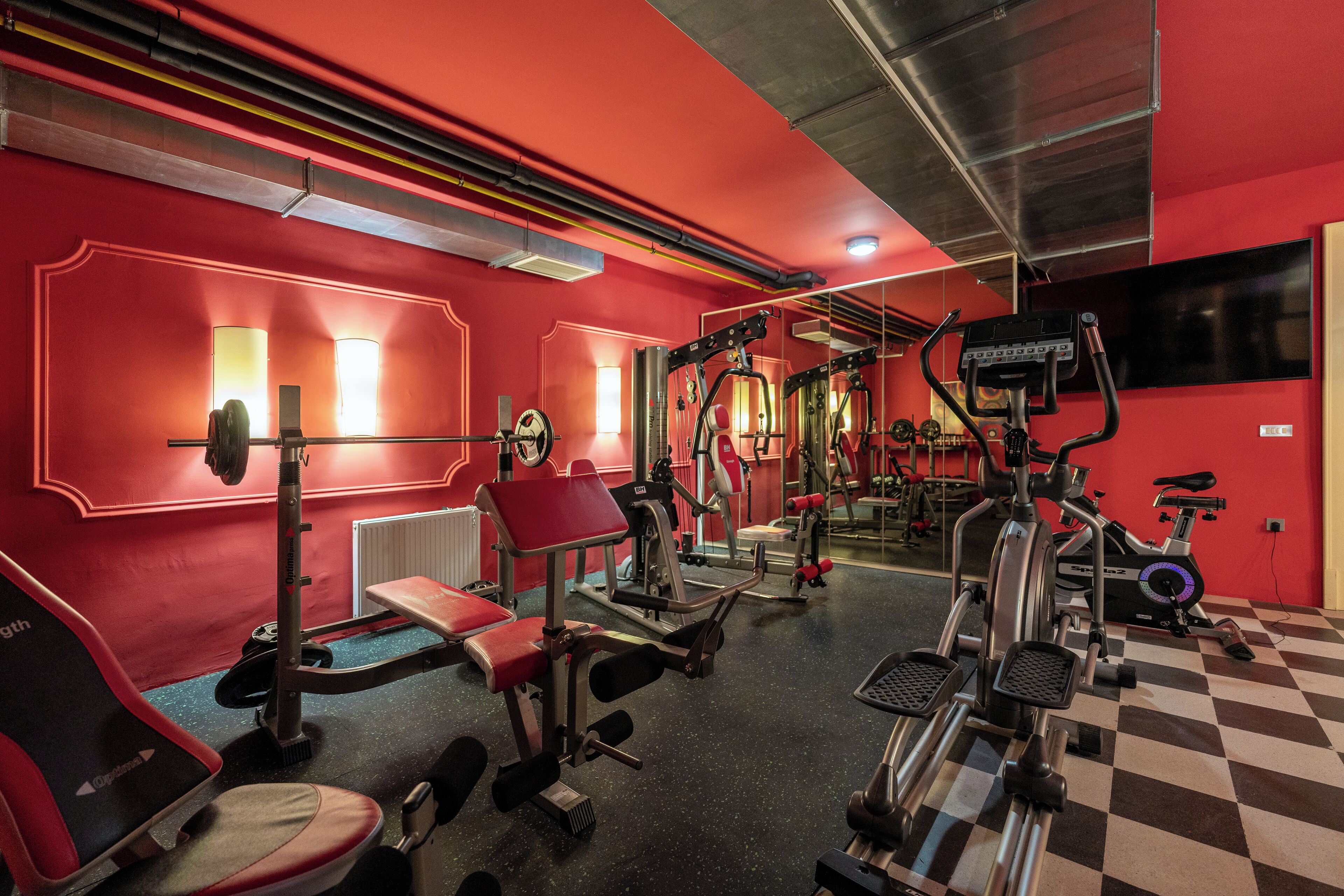 Una palestra con pareti rosse, diverse attrezzature per l'allenamento e un pavimento a scacchi.