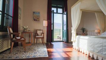 A bedroom with a canopy bed, a wooden floor, a small table with chairs, and a view through an open door.