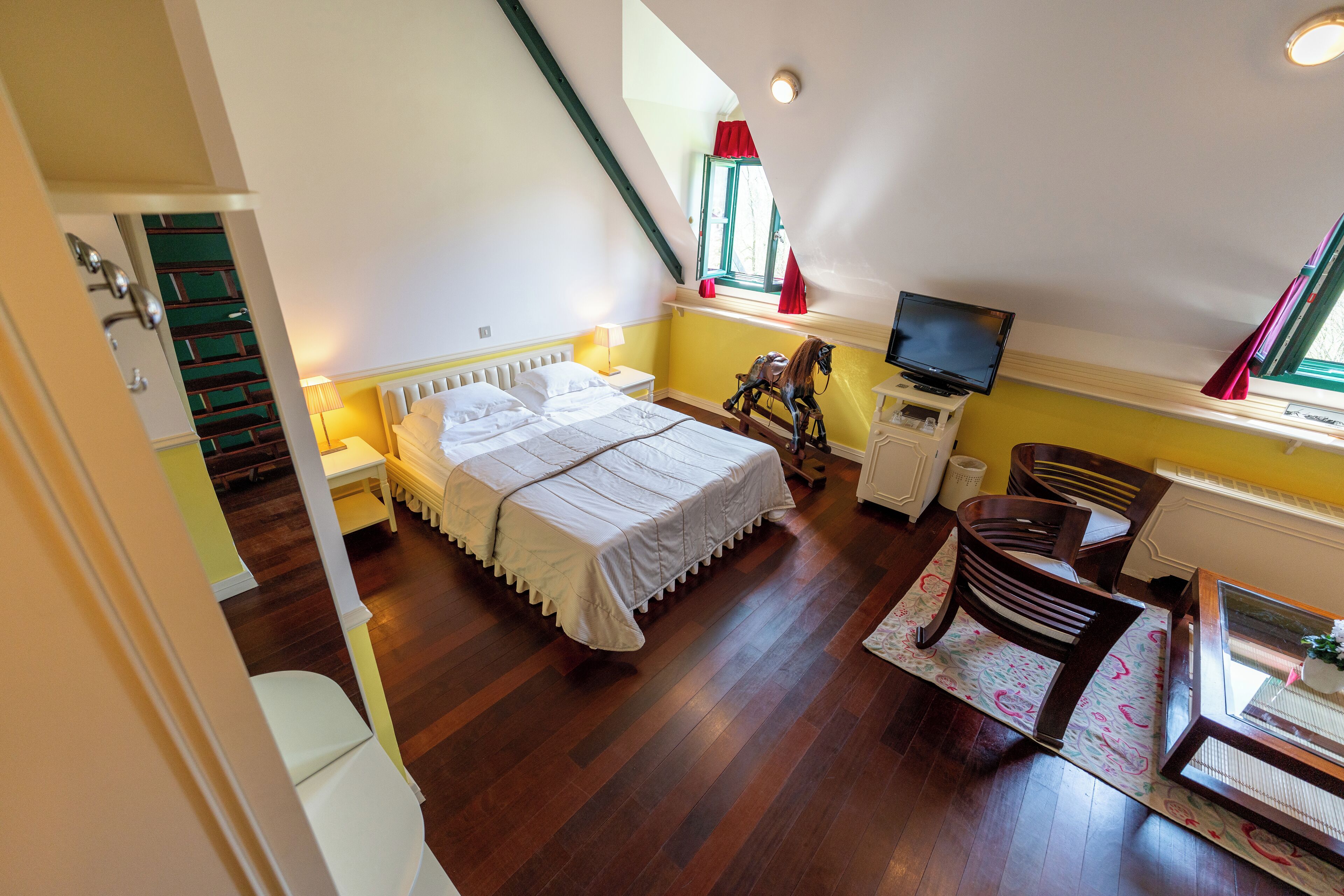 A bedroom with a bed, a television, a window with curtains, and a wooden floor.