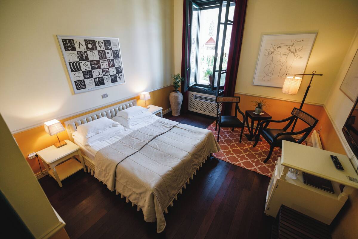A bedroom with a large bed, bedside tables, a chair, a desk, and a window with curtains.
