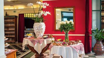 Vestíbulo de hotel con suelo a cuadros, paredes rojas y dos mesas con centros de mesa florales y exhibiciones de comida.