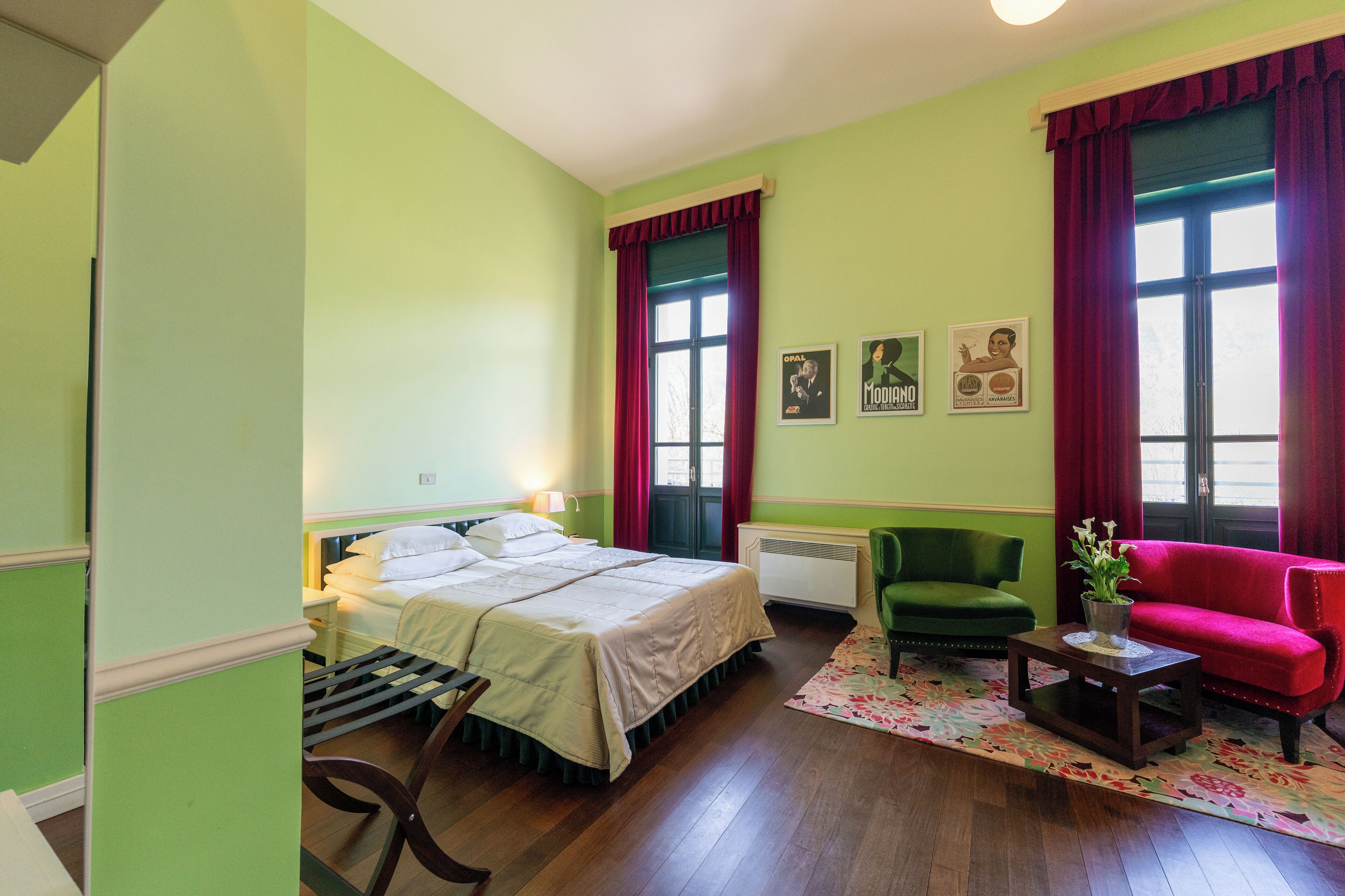 A room with a bed, a green armchair, a red sofa, and a small table with a plant.