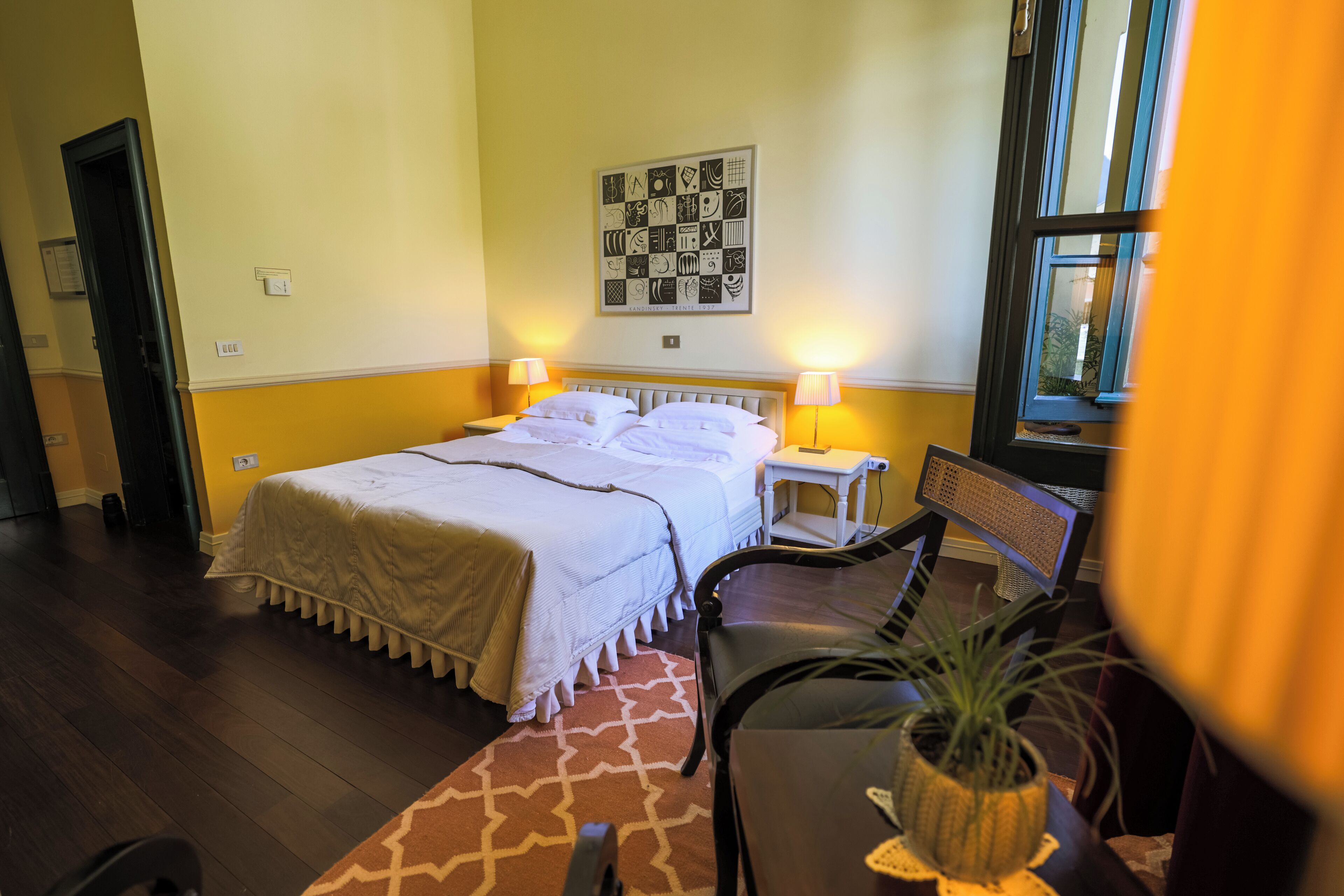 Een hotelkamer met een bed, bedlampjes, een tafeltje met een plant en een raam.