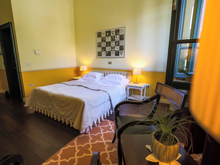 Habitación de hotel con cama, lámparas de noche, una mesita con una planta y una ventana.