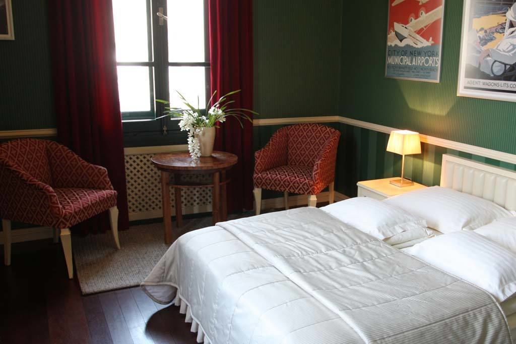 Et hotelværelse med en seng, to møbelstole med mønster, et lille bord med en vase og et billede på væggen.