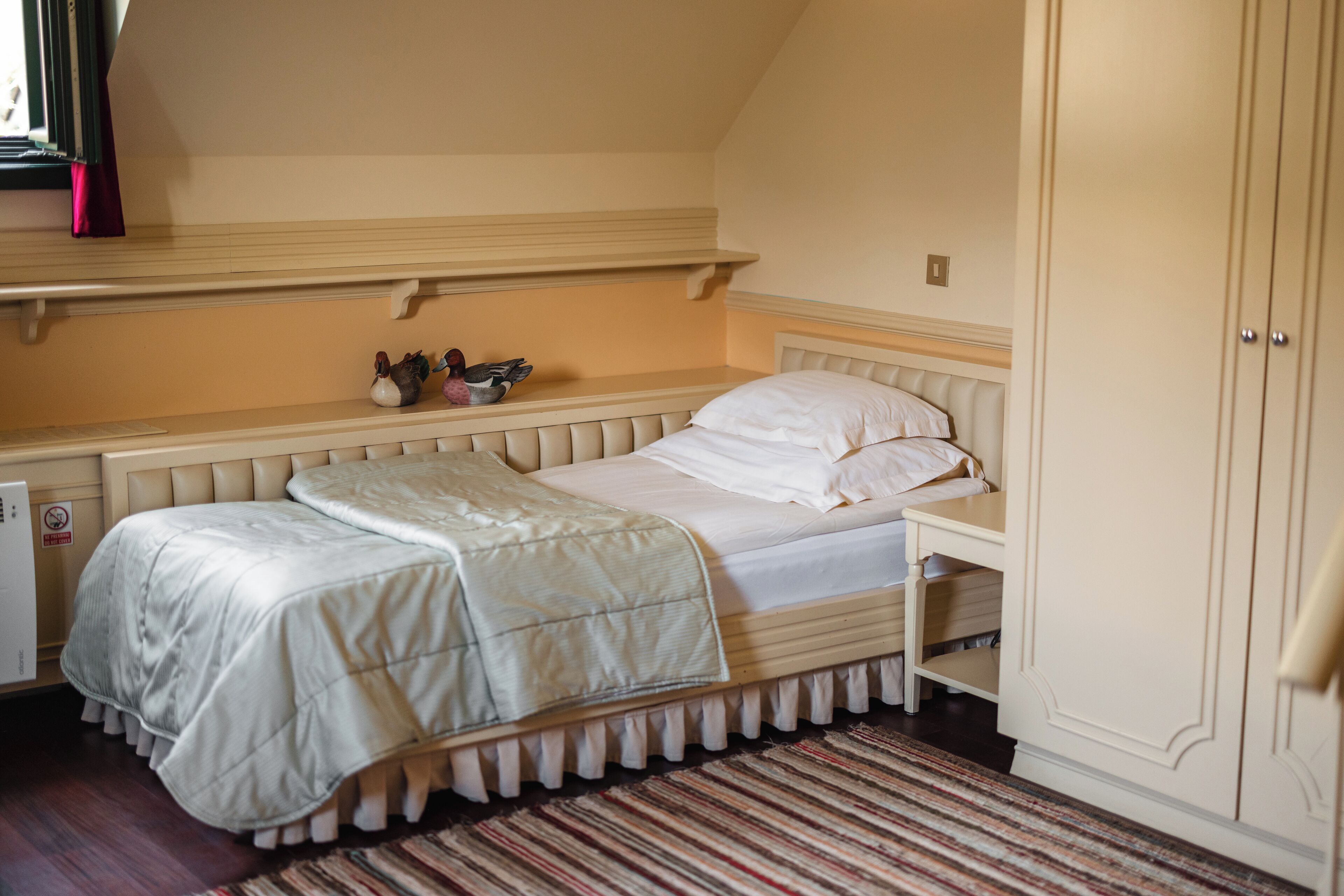 Ein Schlafzimmer mit einem Einzelbett, einem Nachttisch, einer Kommode und einem Fenster mit Vorhängen.