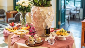 Una mesa de comedor con piso a cuadros, un jarrón con orquídeas blancas y diversos alimentos.