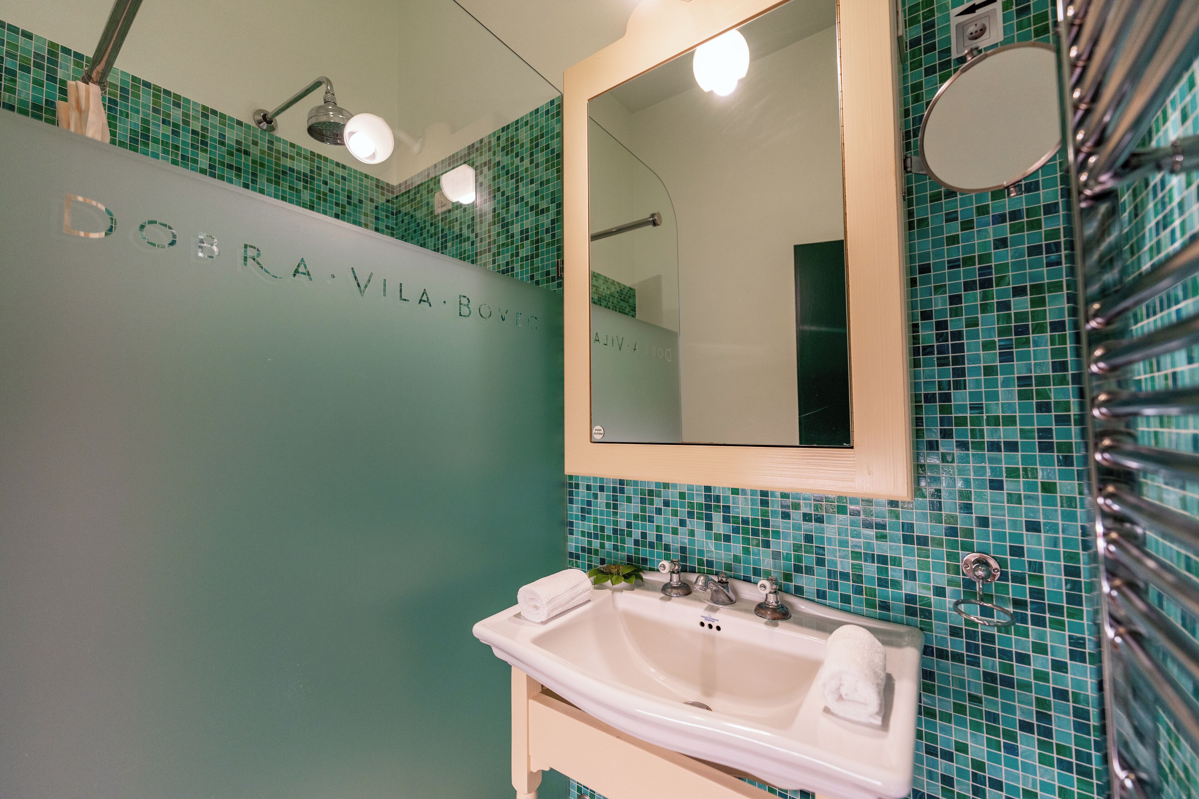A bathroom with a sink, mirror, and green mosaic tiles.
