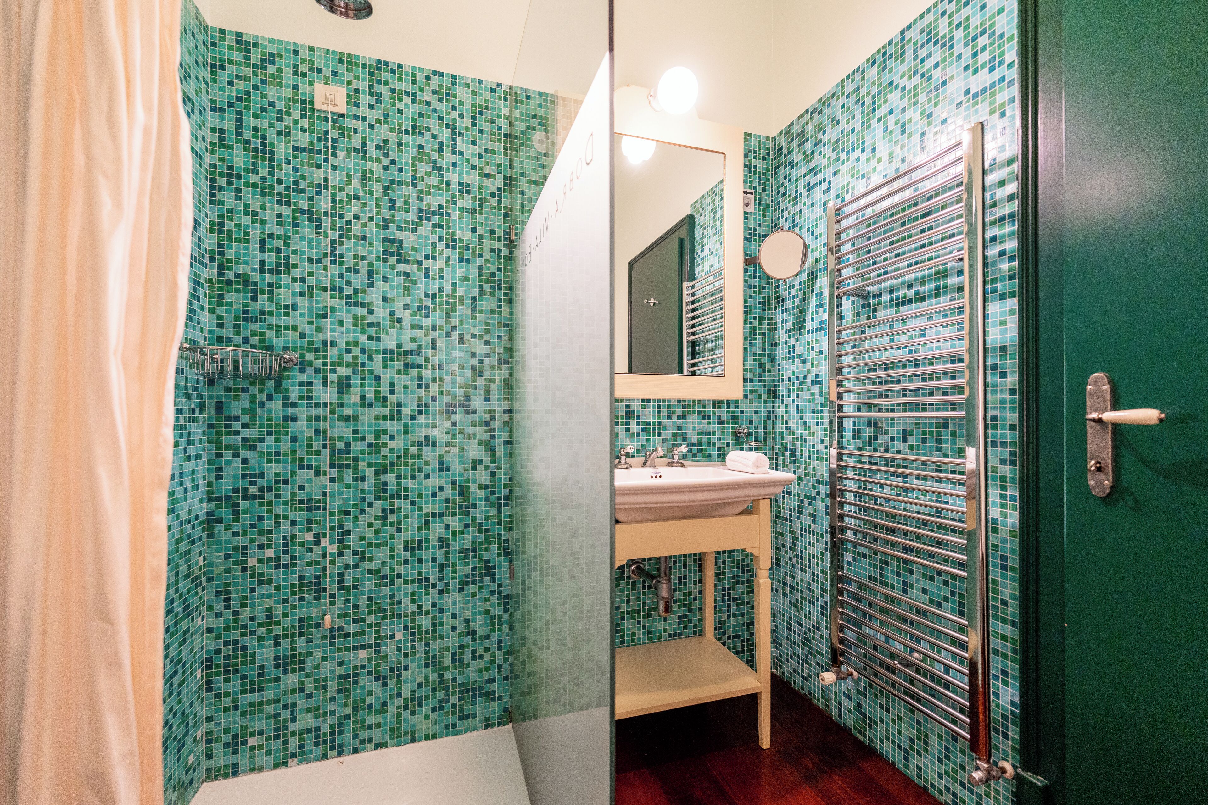 Un baño con pared de azulejos, un lavamanos, un espejo y un perchero para toallas.