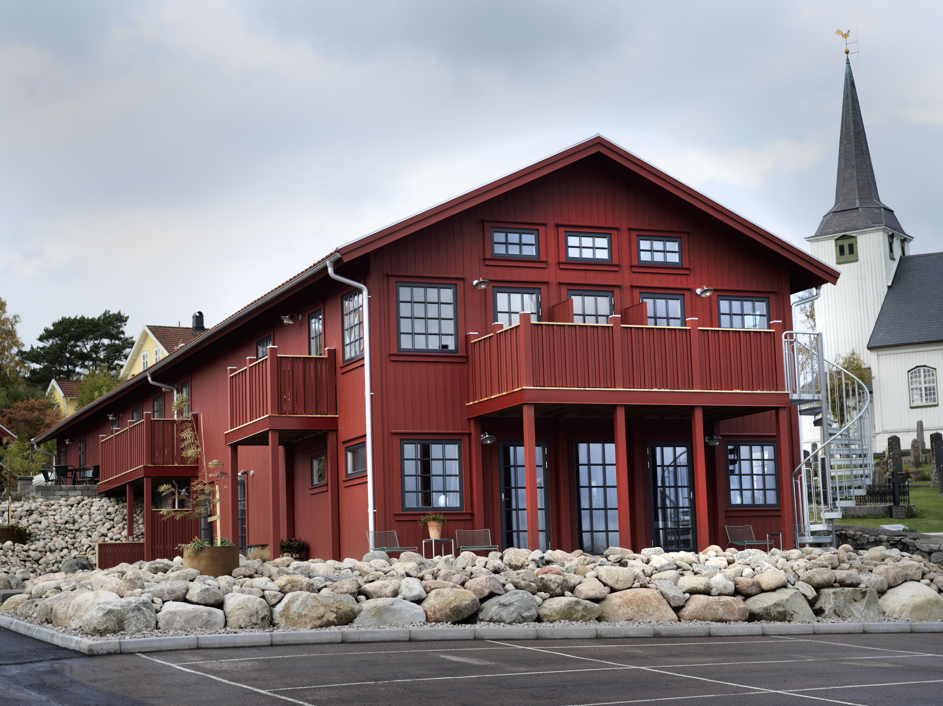 A red building with multiple windows and balconies, surrounded by a stone wall and a parking lot.