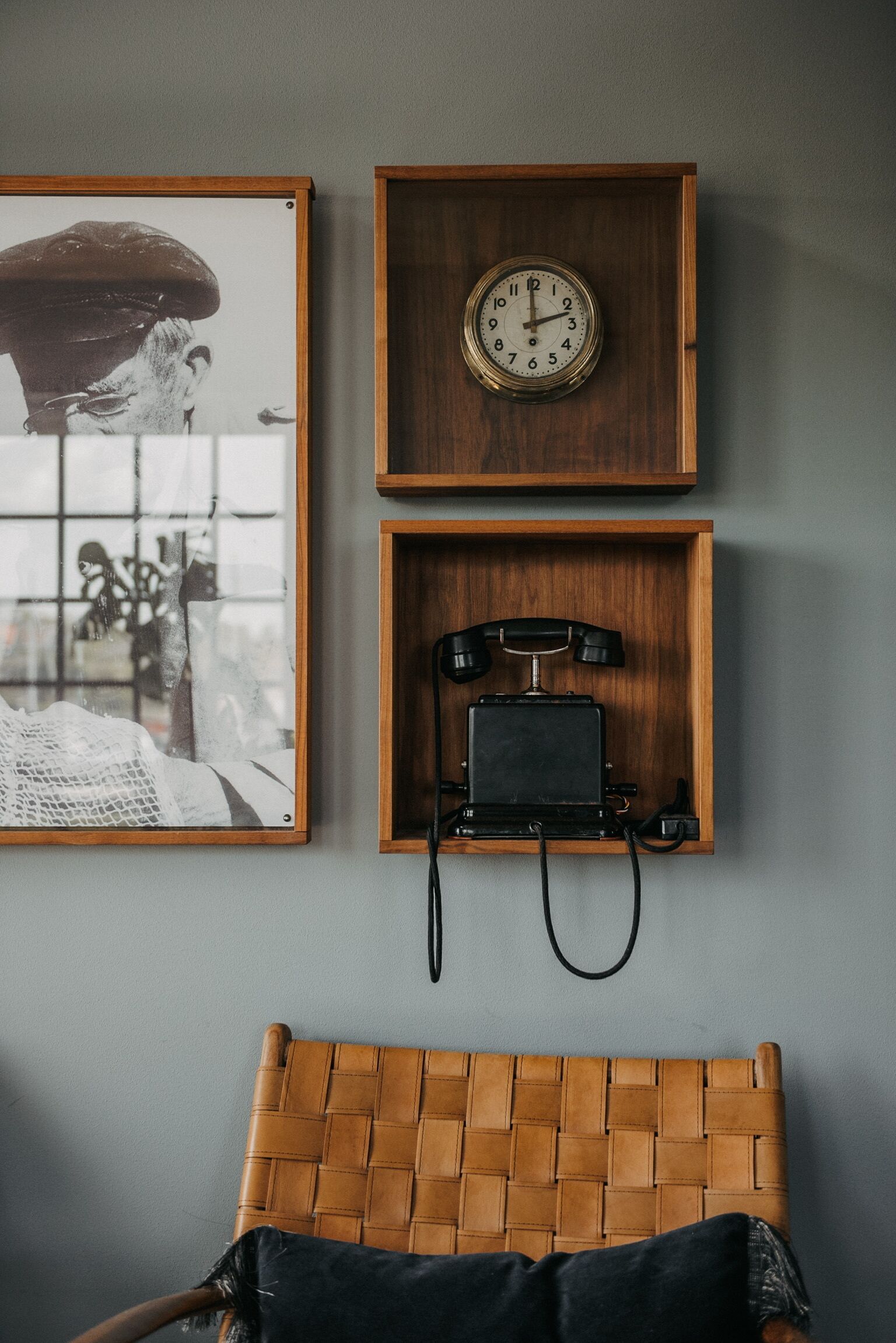 Une étagère en bois fixée au mur, ornée d’une horloge, d’un téléphone ancien et d’un tableau encadré.