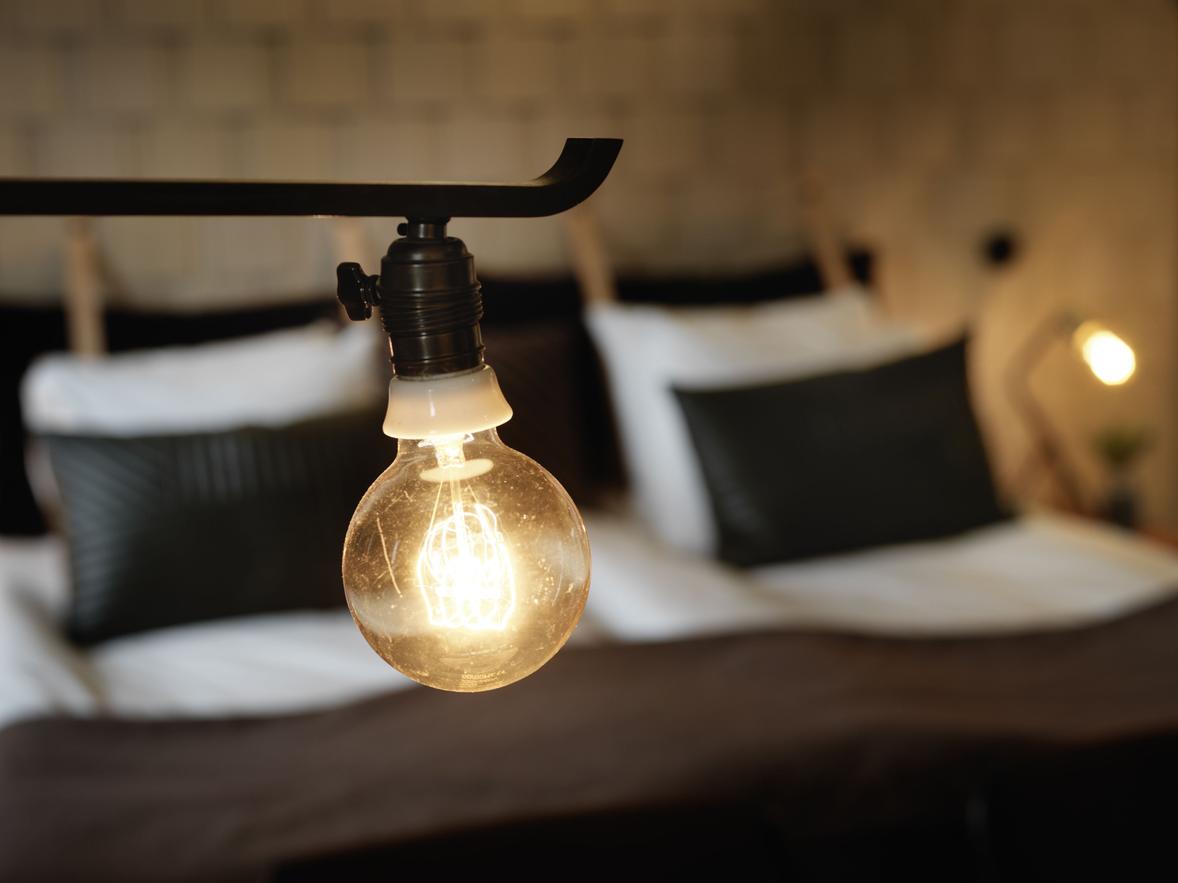A hanging light bulb in a room with a bed and pillows.